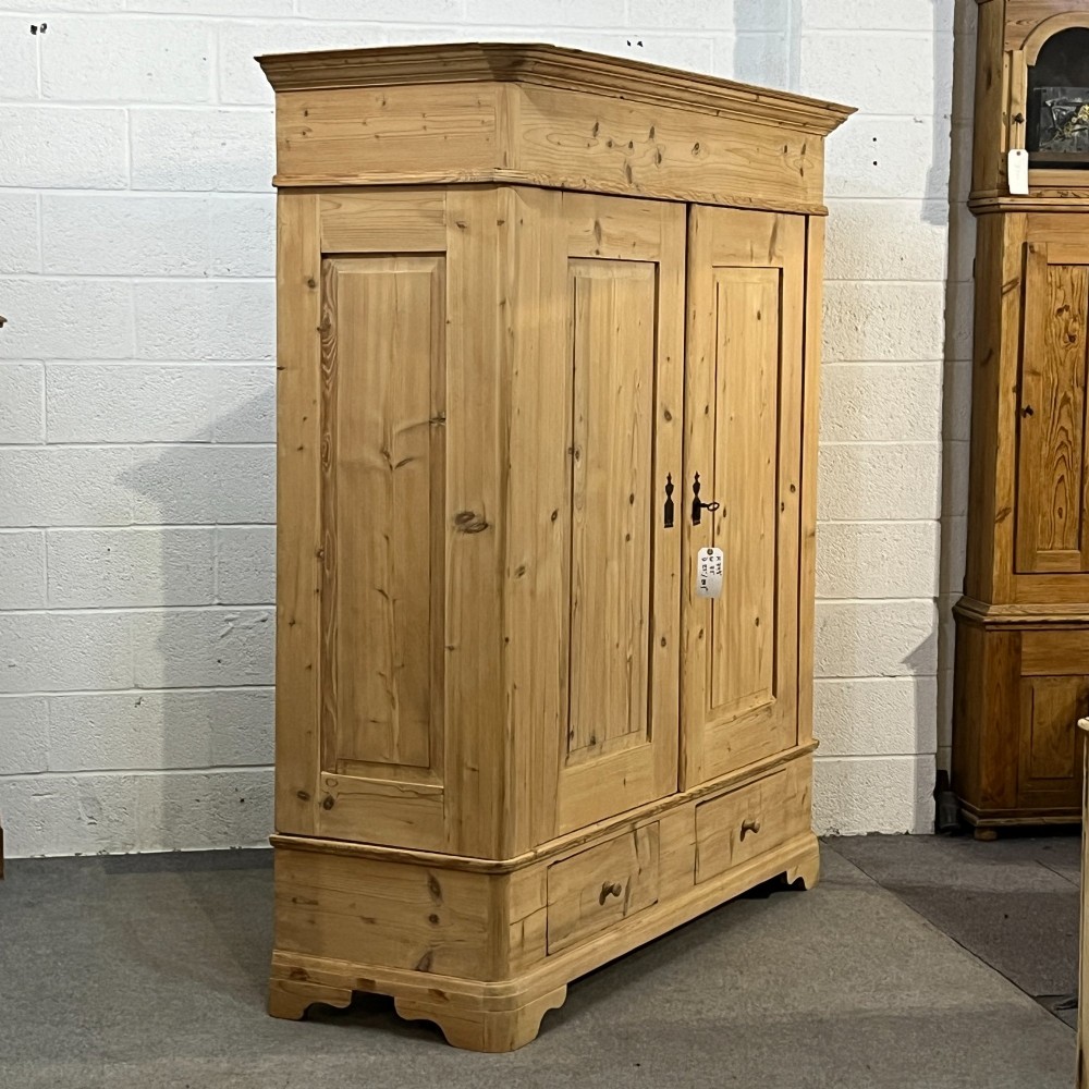 A large Victorian pine double wardrobe featuring fielded panel doors, iron escutcheons, and two base drawers on a plinth foundation. View III