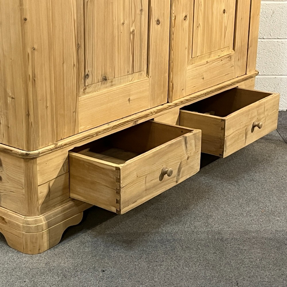 A large Victorian pine double wardrobe featuring fielded panel doors, iron escutcheons, and two base drawers on a plinth foundation. View IV