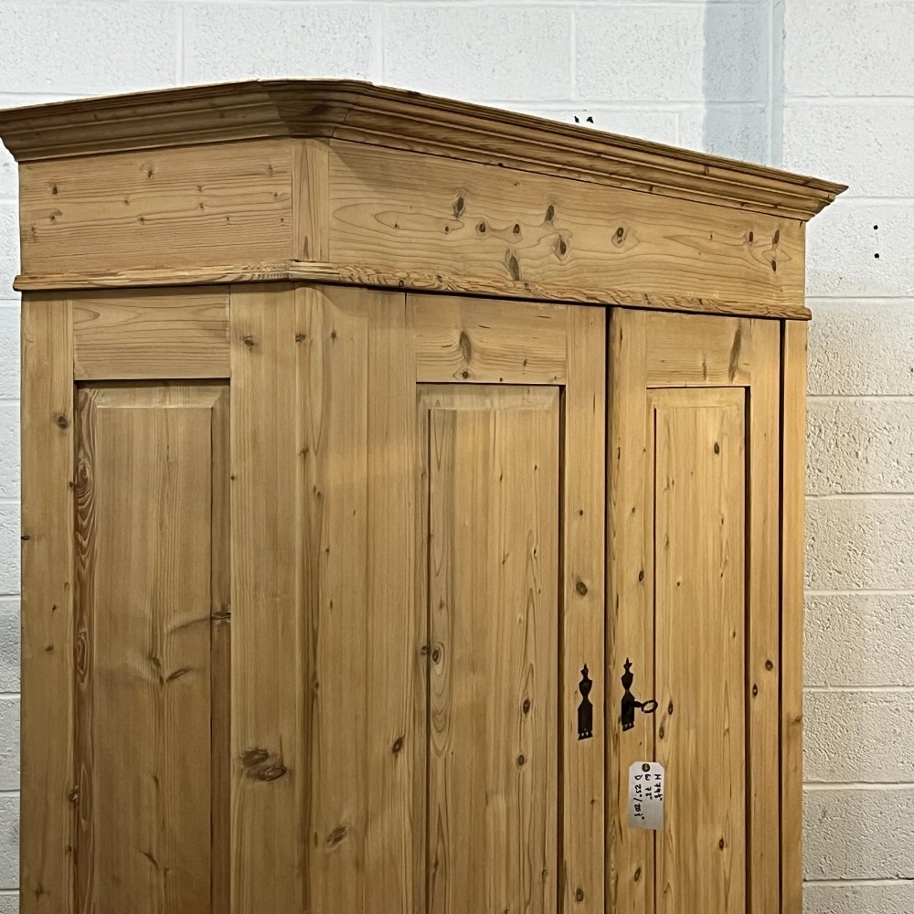 A large Victorian pine double wardrobe featuring fielded panel doors, iron escutcheons, and two base drawers on a plinth foundation. View V