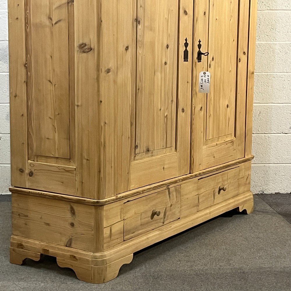 A large Victorian pine double wardrobe featuring fielded panel doors, iron escutcheons, and two base drawers on a plinth foundation. View VI