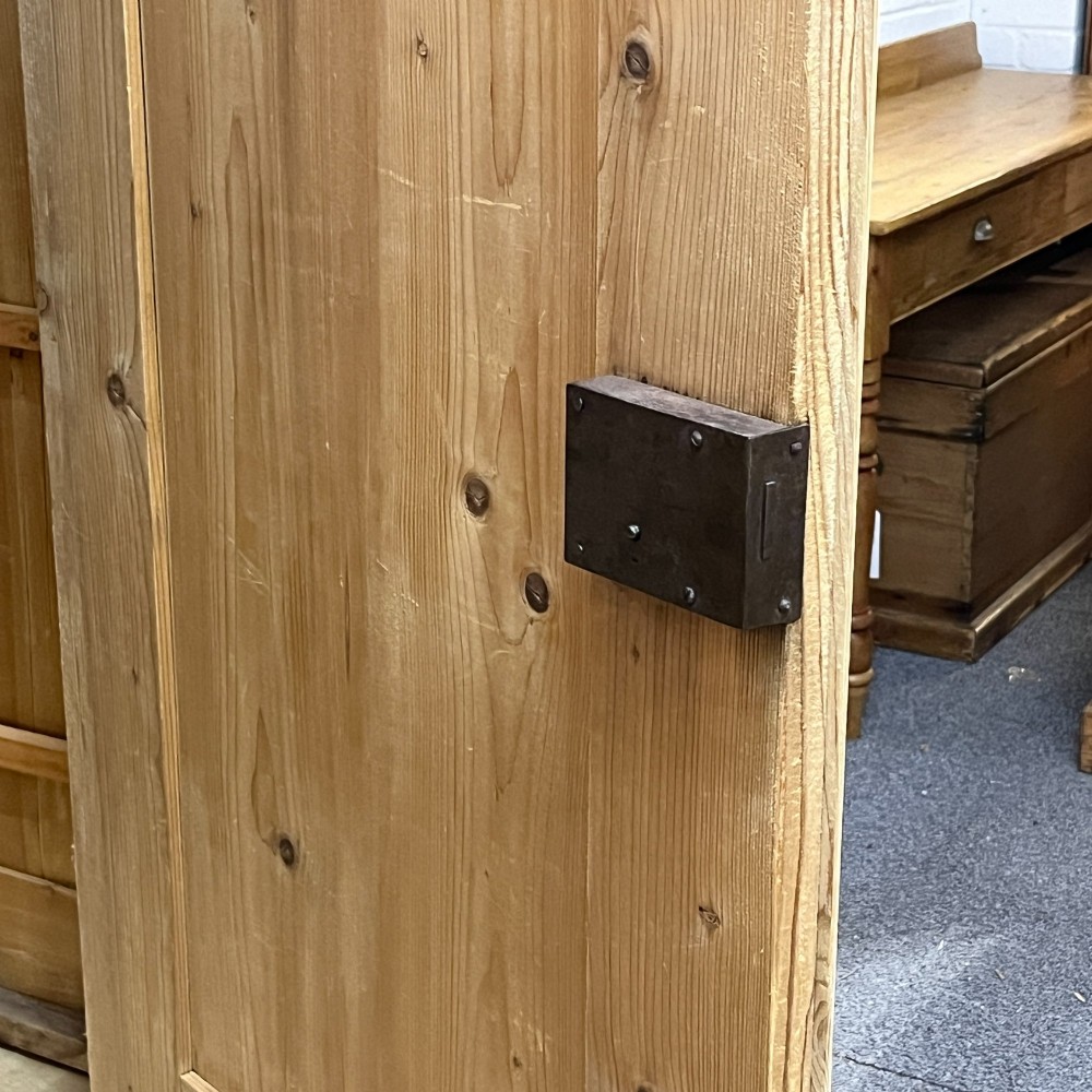 A large Victorian pine double wardrobe featuring fielded panel doors, iron escutcheons, and two base drawers on a plinth foundation. View XI