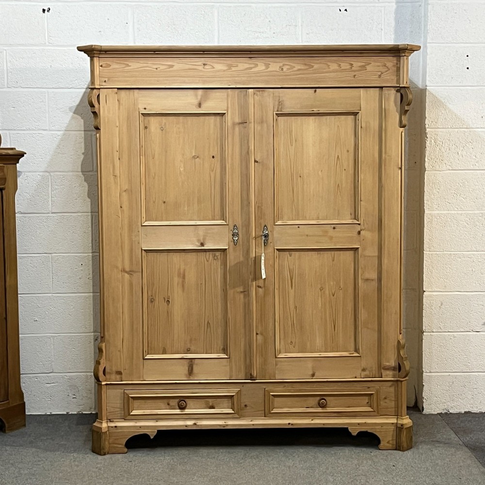 A large antique pine double wardrobe featuring panelled doors, two bottom drawers with turned handles, and a moulded top cornice.