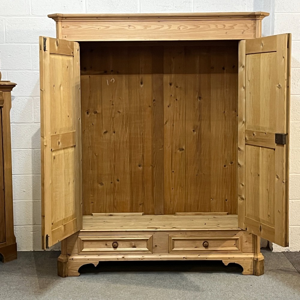 A large antique pine double wardrobe featuring panelled doors, two bottom drawers with turned handles, and a moulded top cornice. View IV
