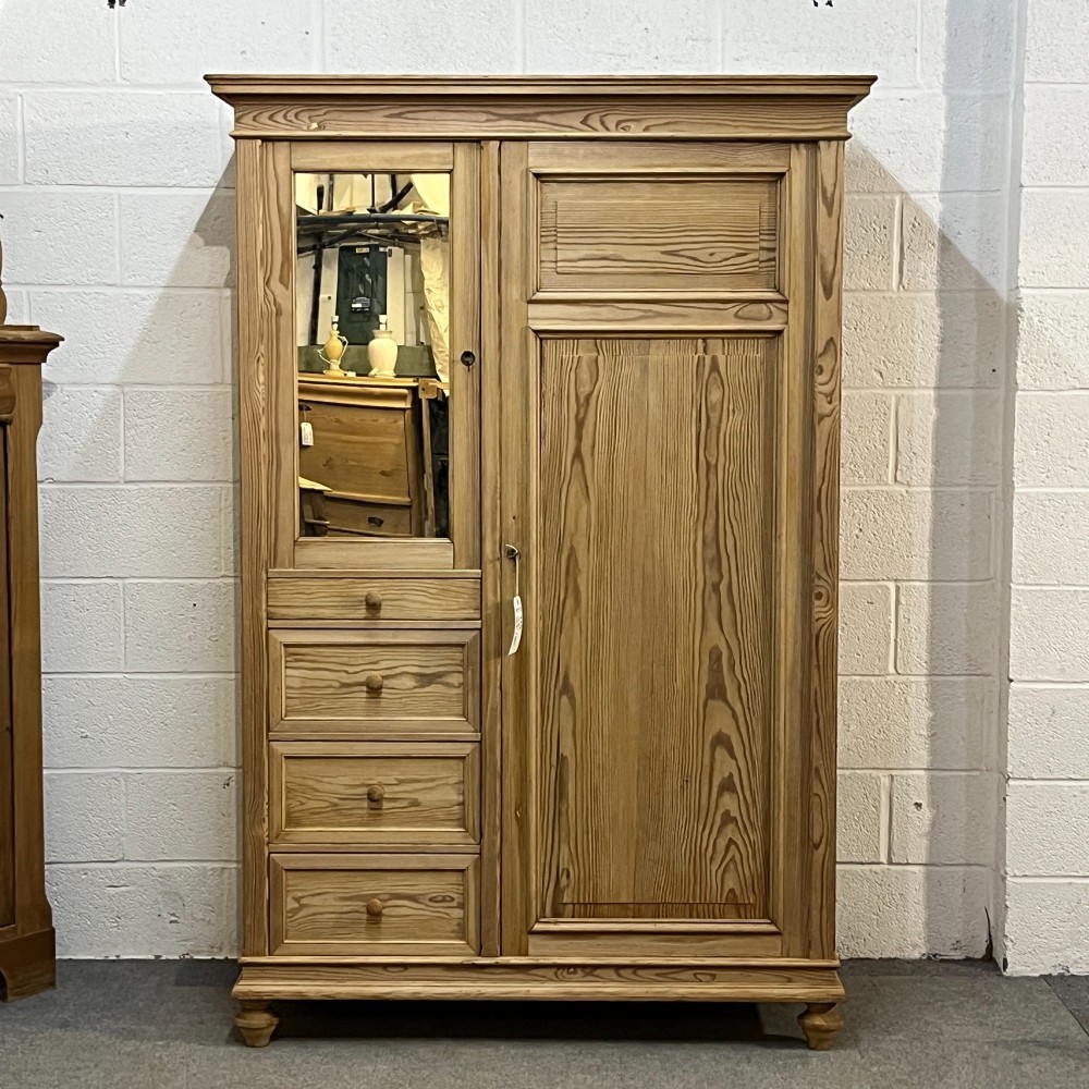 A freestanding 1930s pine compactum wardrobe featuring a upper mirror above four drawers on the left and a tall panelled door on the right.