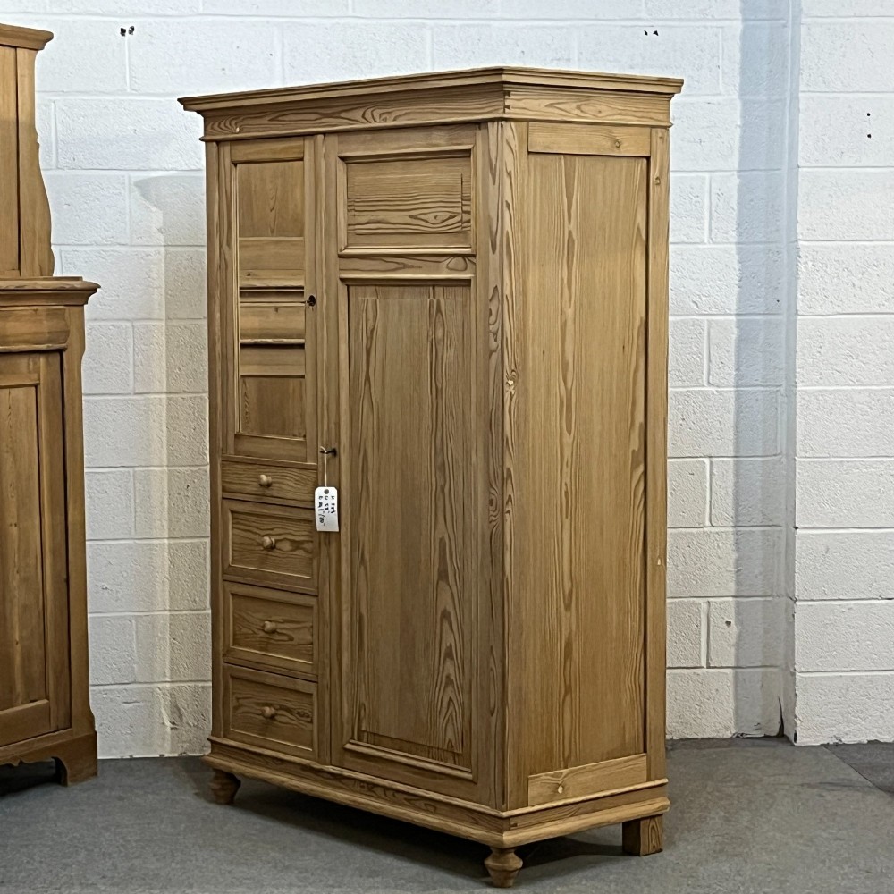 A freestanding 1930s pine compactum wardrobe featuring a upper mirror above four drawers on the left and a tall panelled door on the right. View II