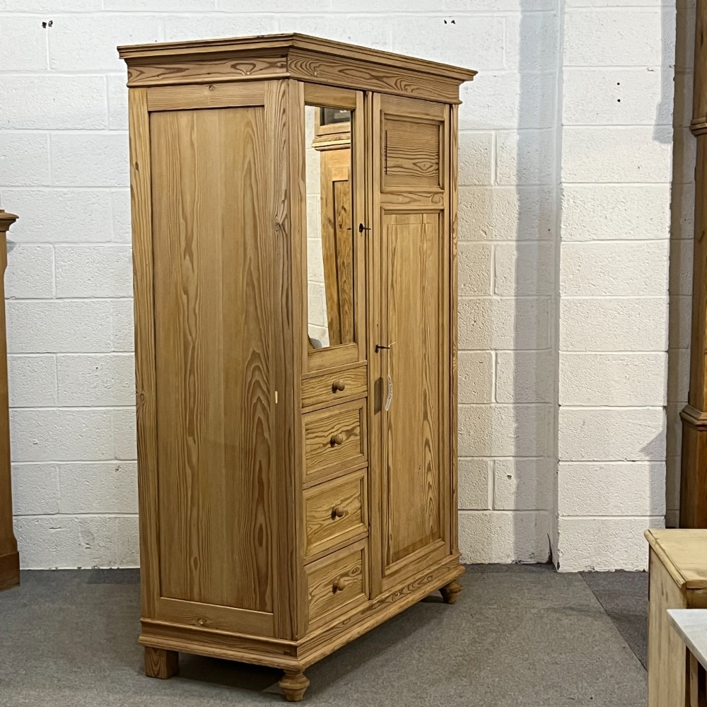 A freestanding 1930s pine compactum wardrobe featuring a upper mirror above four drawers on the left and a tall panelled door on the right. View III