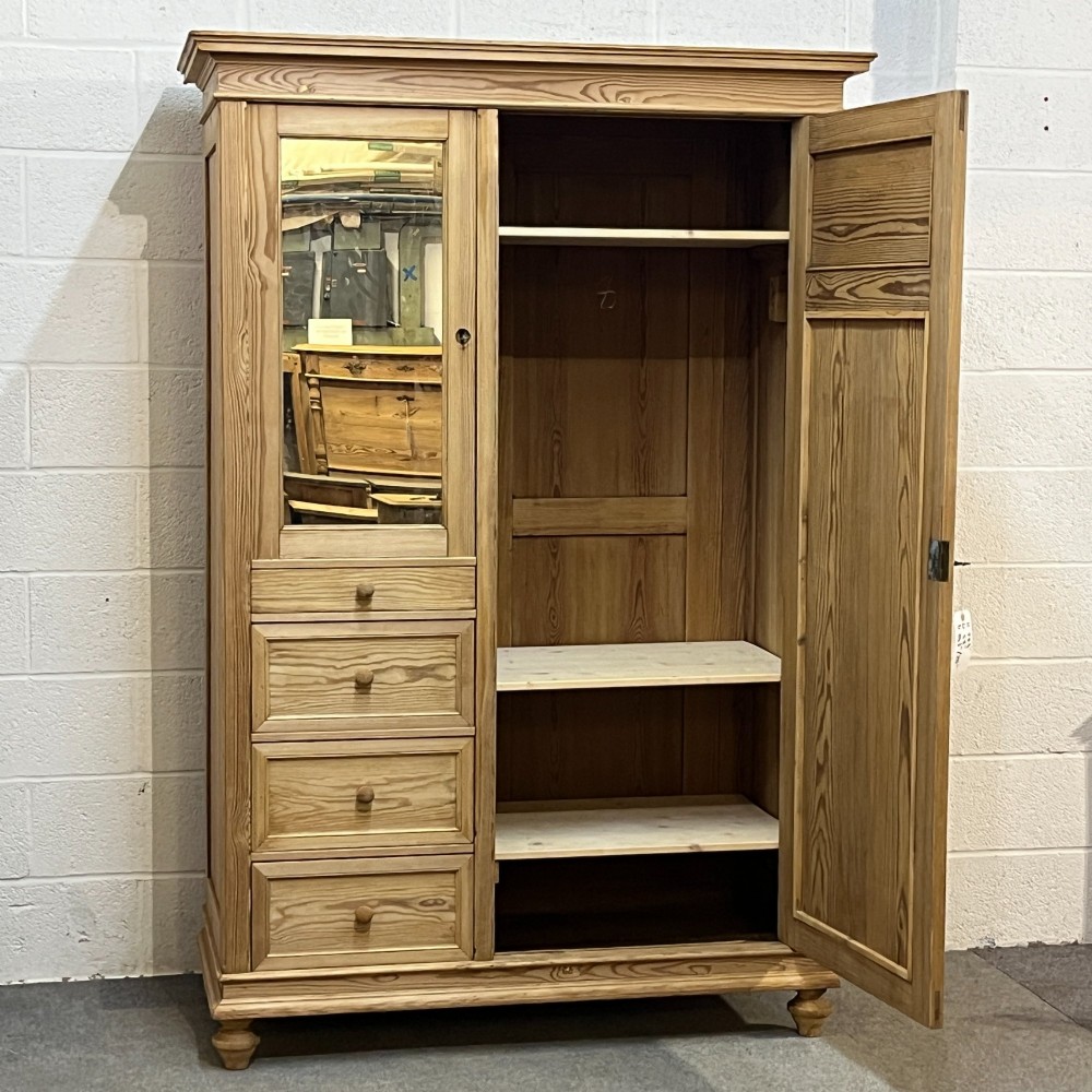 A freestanding 1930s pine compactum wardrobe featuring a upper mirror above four drawers on the left and a tall panelled door on the right. View IV