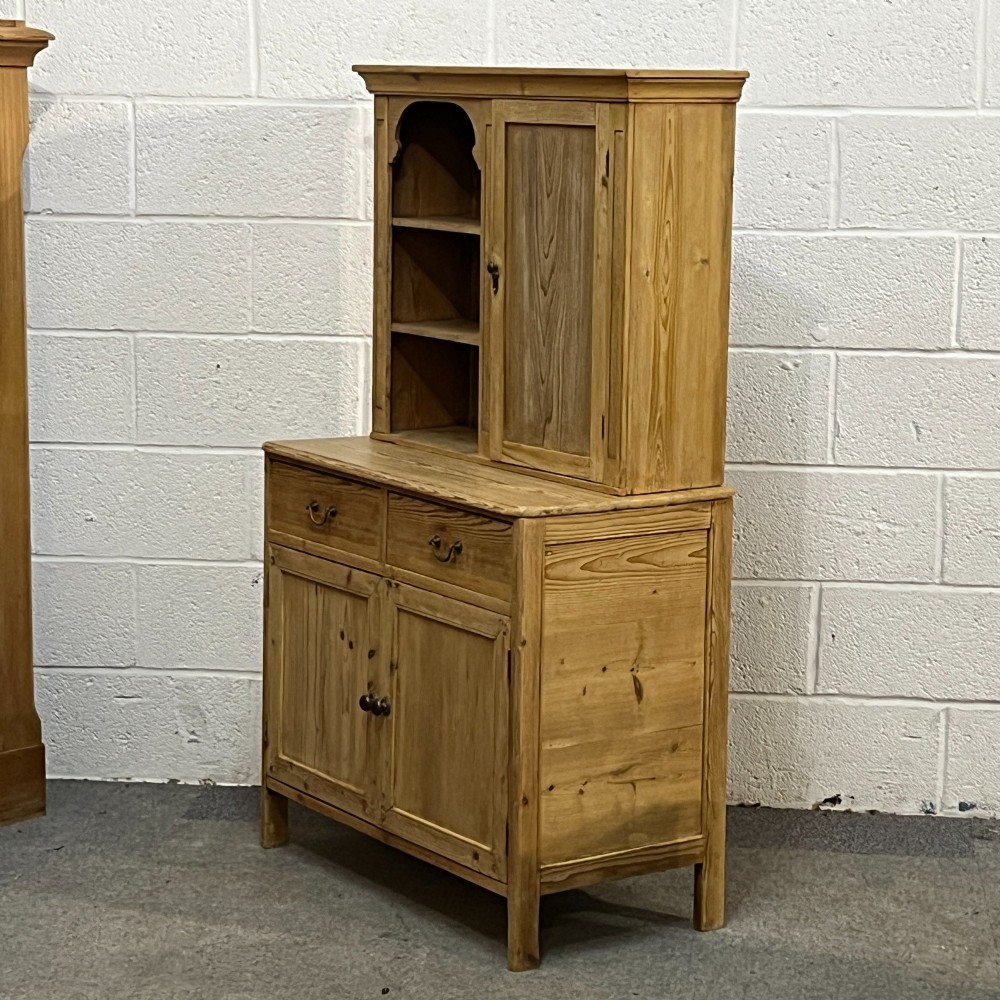 A small antique pine kitchen dresser featuring an upper rack with arched open shelves and a single cupboard door above a base unit with two drawers and two panelled doors. View II
