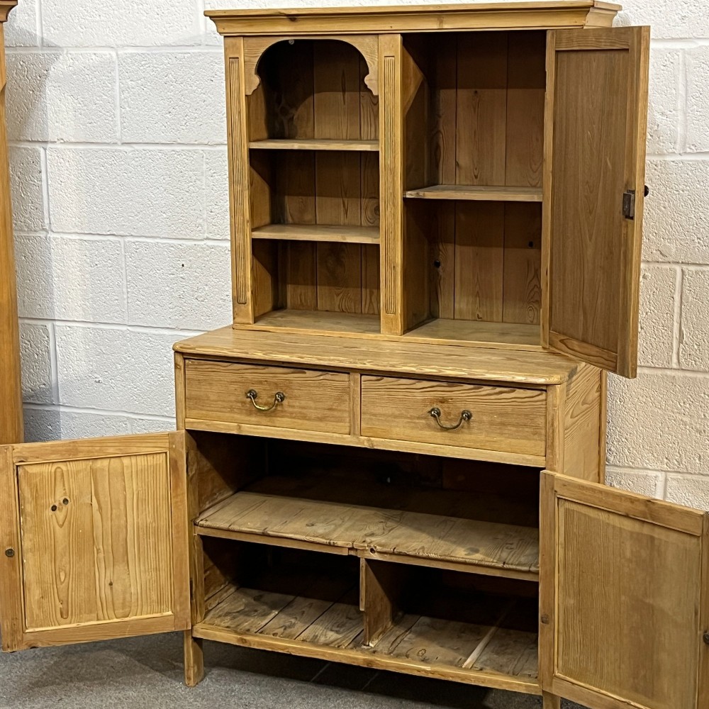 A small antique pine kitchen dresser featuring an upper rack with arched open shelves and a single cupboard door above a base unit with two drawers and two panelled doors. View V