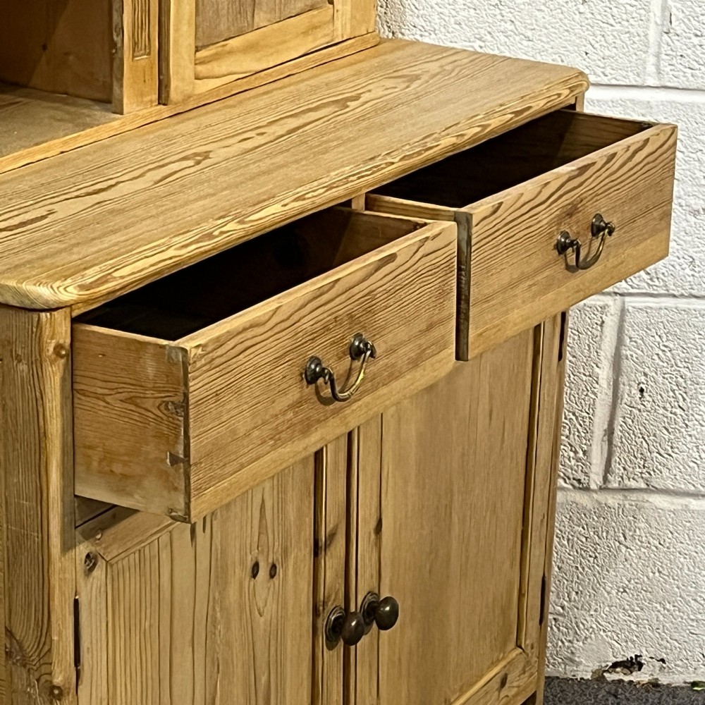 A small antique pine kitchen dresser featuring an upper rack with arched open shelves and a single cupboard door above a base unit with two drawers and two panelled doors. View VI