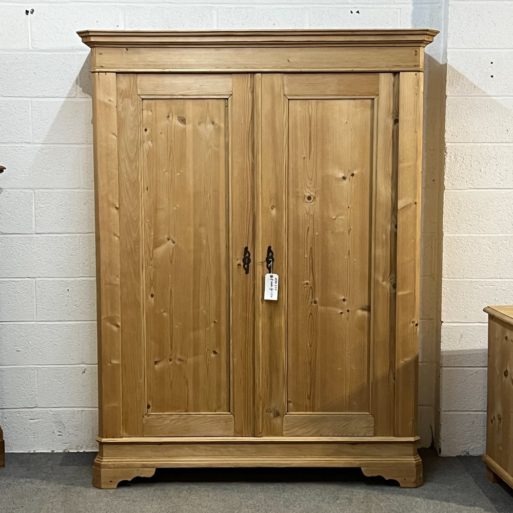 A large two-door antique pine wardrobe with fielded panels, a plain stepped cornice, moulding at the base, and central iron escutcheons.