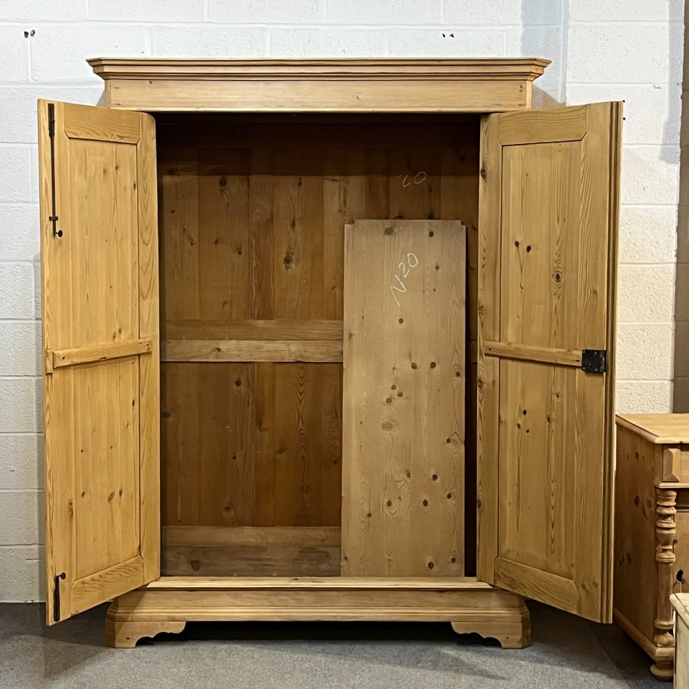 A large two-door antique pine wardrobe with fielded panels, a plain stepped cornice, moulding at the base, and central iron escutcheons. View II