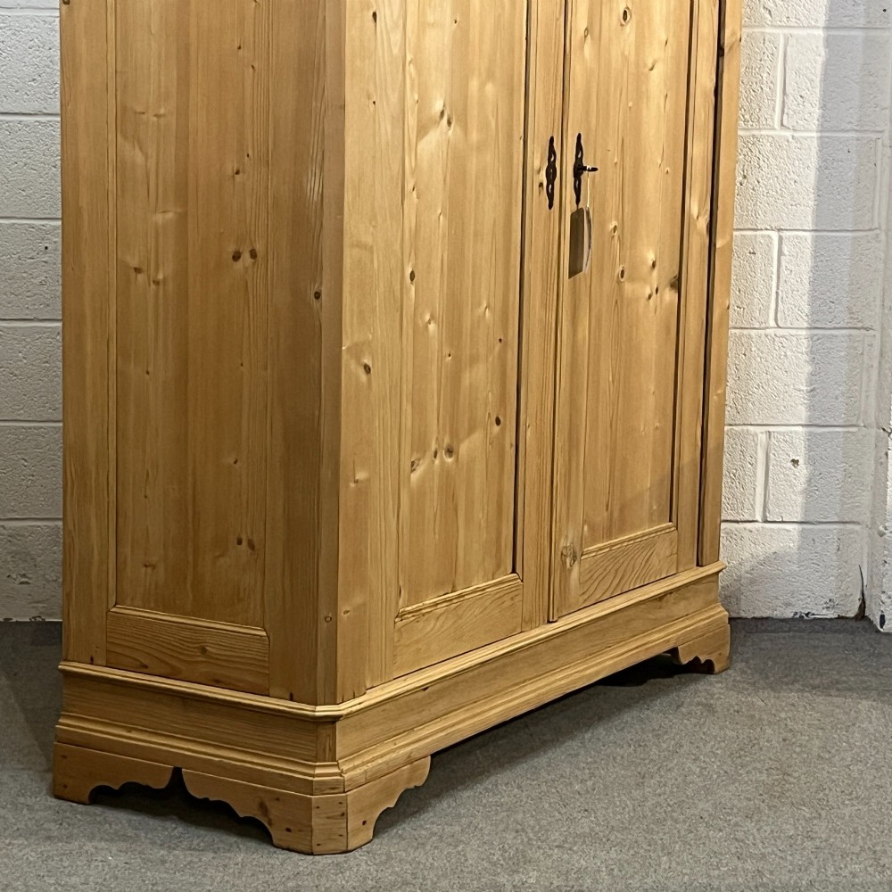 A large two-door antique pine wardrobe with fielded panels, a plain stepped cornice, moulding at the base, and central iron escutcheons. View V