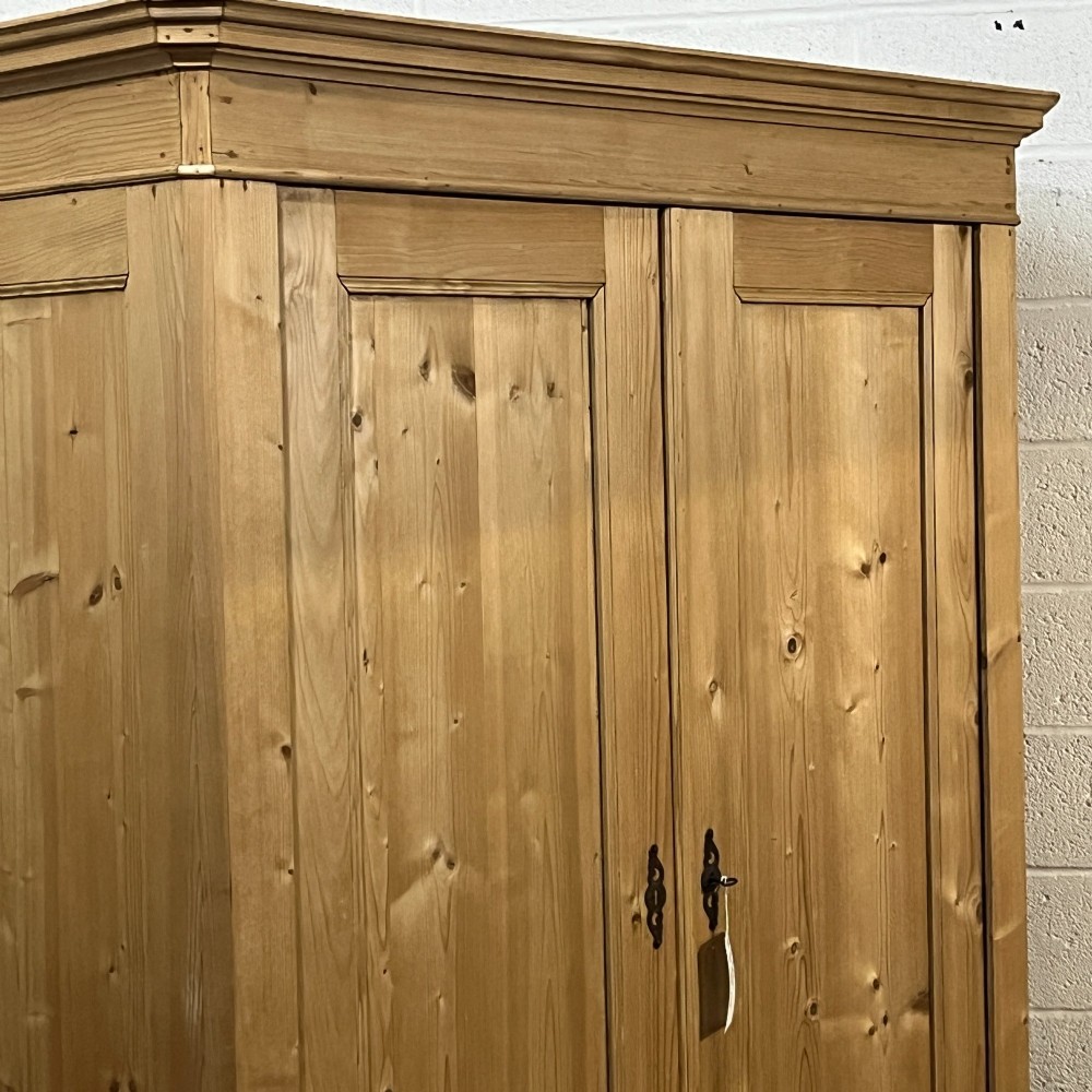 A large two-door antique pine wardrobe with fielded panels, a plain stepped cornice, moulding at the base, and central iron escutcheons. View VI