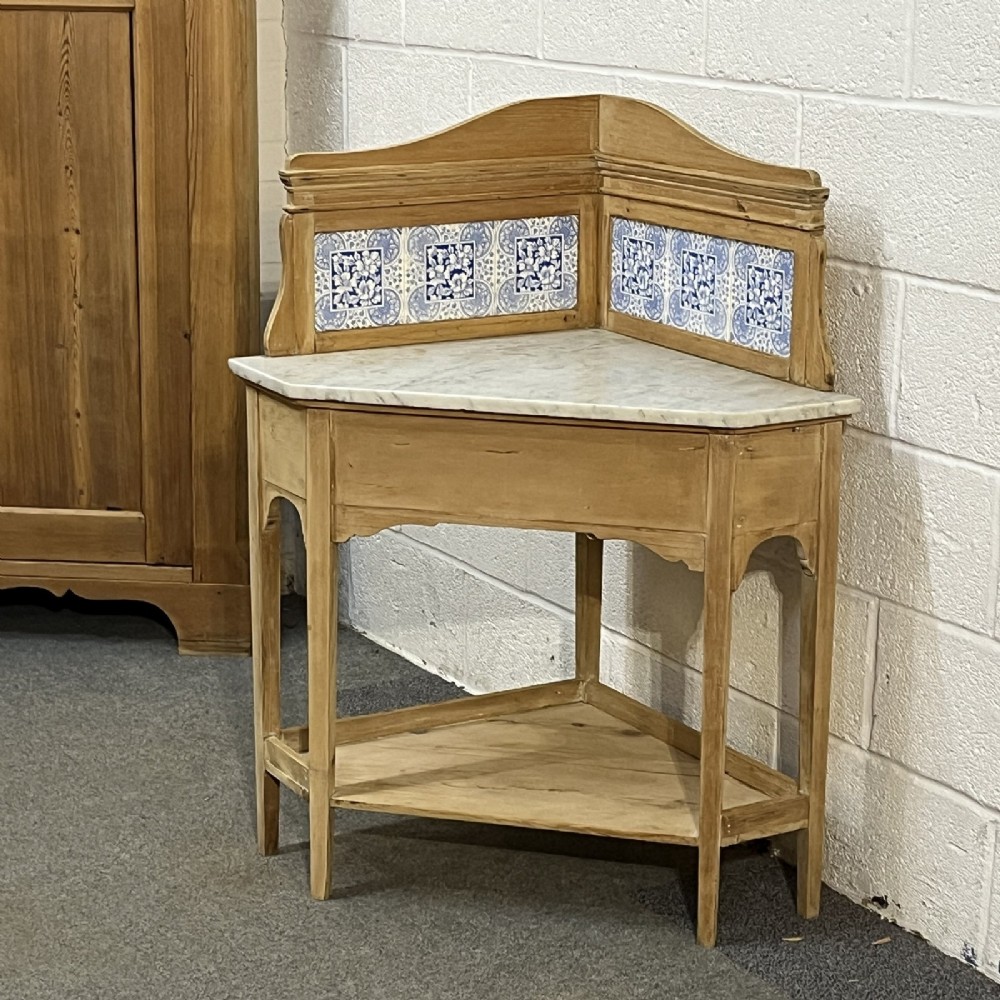 A Victorian corner washstand constructed from natural pine, featuring a grey-veined marble top, blue and white tiled splashback, and a lower triangular shelf. View II