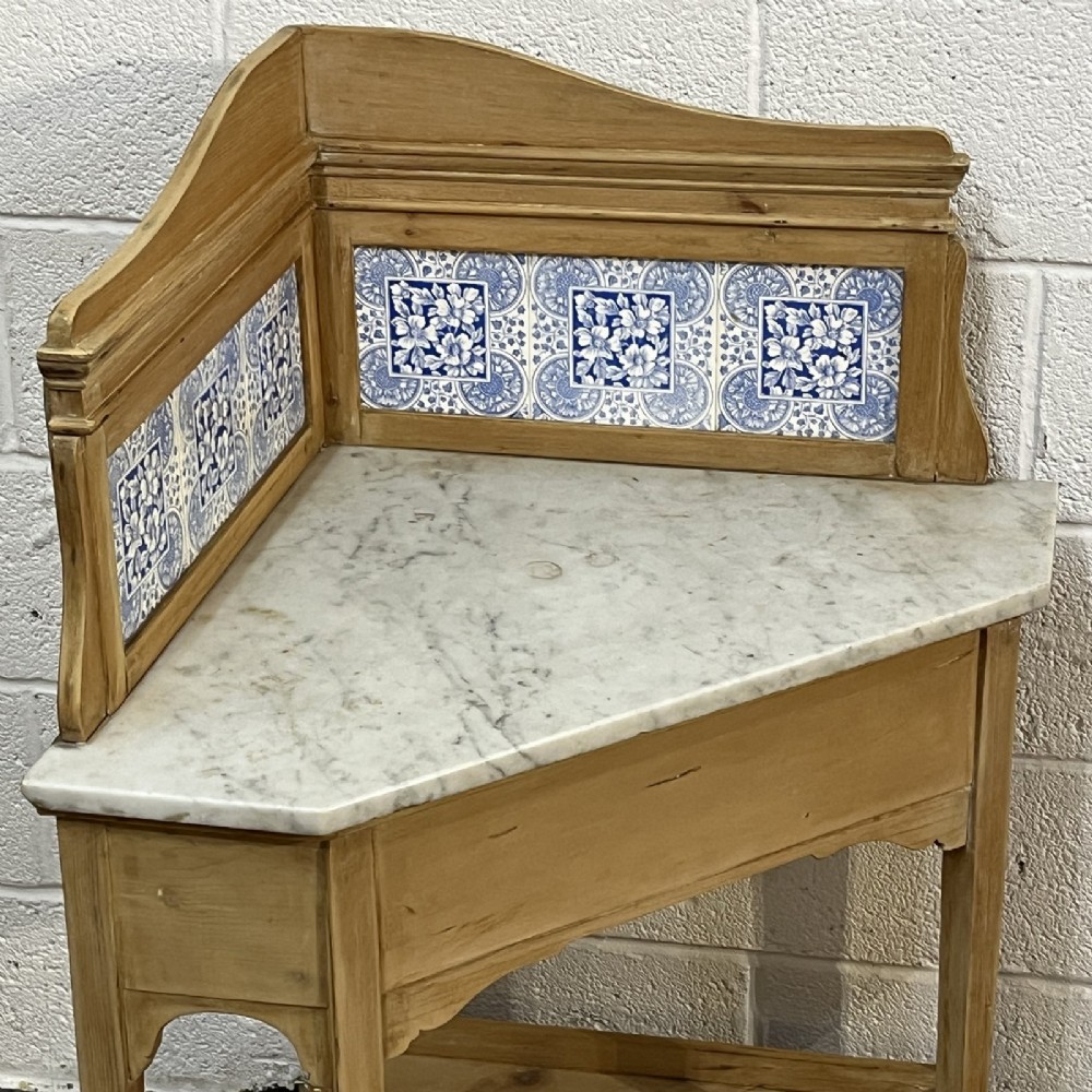 A Victorian corner washstand constructed from natural pine, featuring a grey-veined marble top, blue and white tiled splashback, and a lower triangular shelf. View III