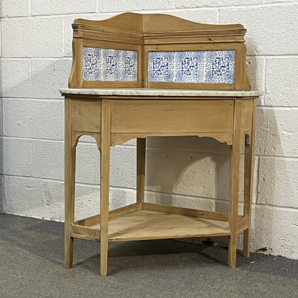 A Victorian corner washstand constructed from natural pine, featuring a grey-veined marble top, blue and white tiled splashback, and a lower triangular shelf. View IV