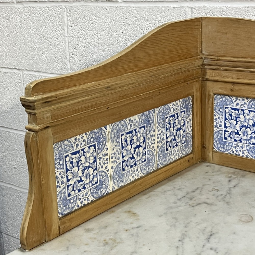 A Victorian corner washstand constructed from natural pine, featuring a grey-veined marble top, blue and white tiled splashback, and a lower triangular shelf. View V