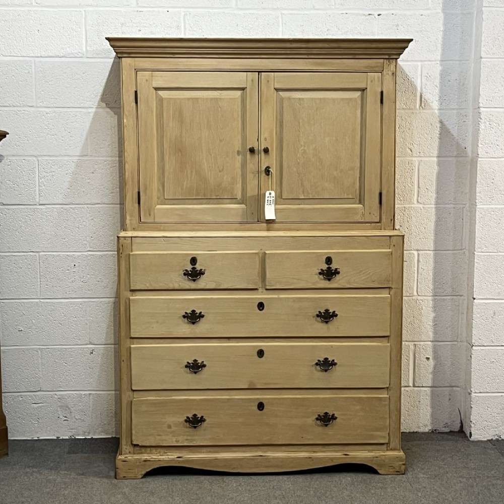 A nineteenth-century pale pine linen press featuring a double-door top cupboard set above two short and three long graduated drawers with brass handles.