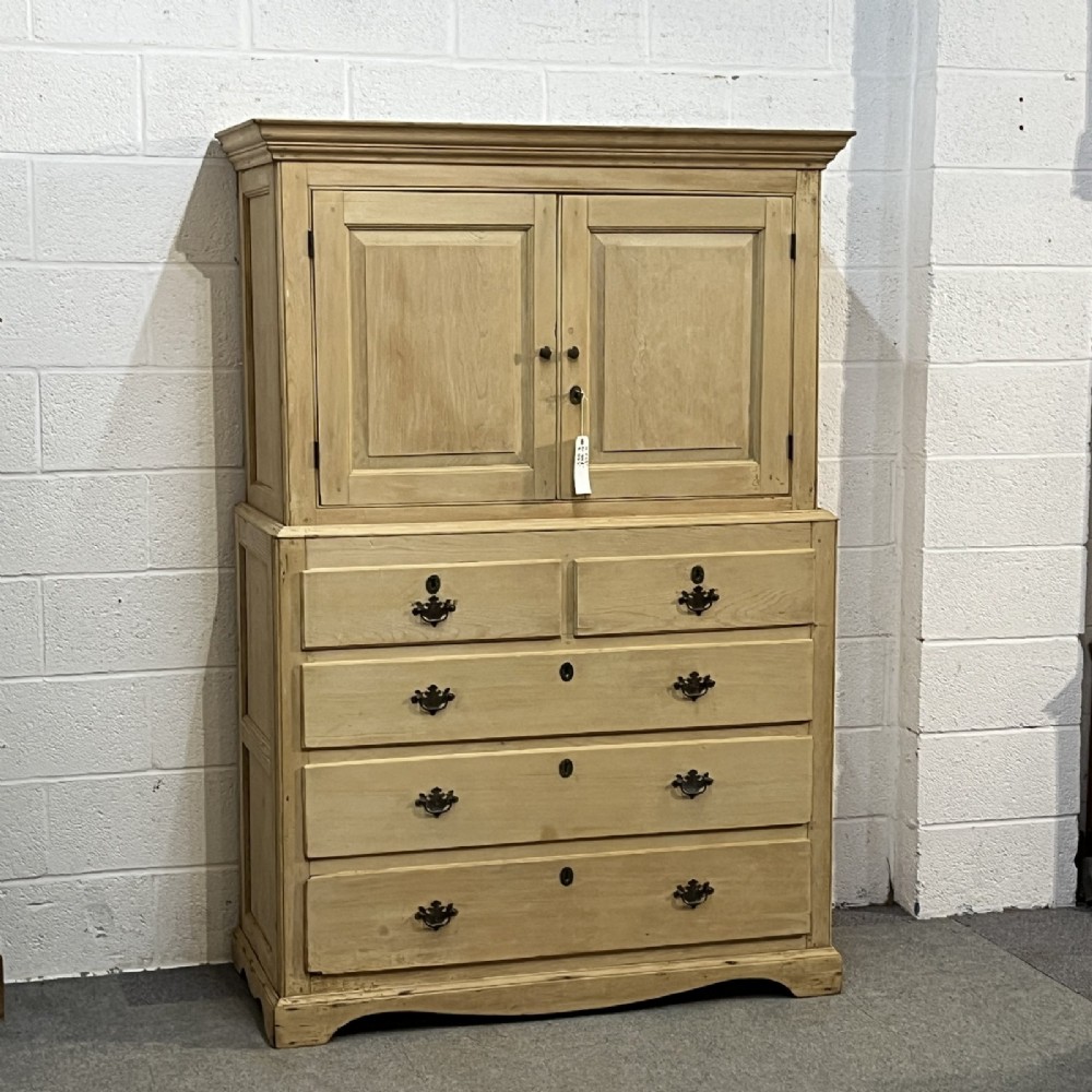 A nineteenth-century pale pine linen press featuring a double-door top cupboard set above two short and three long graduated drawers with brass handles. View IV