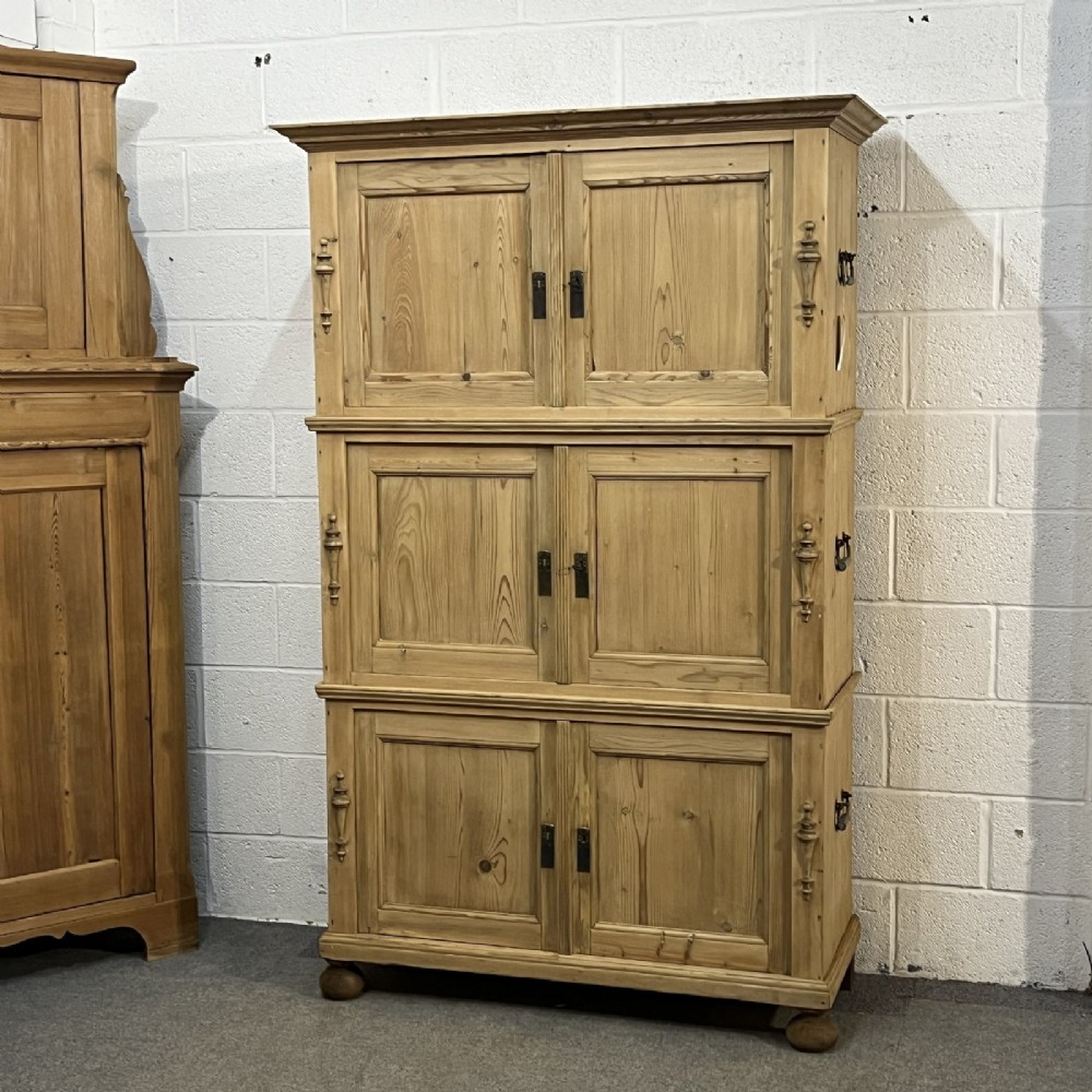 A three-section antique pine campaign cupboard featuring panelled doors, iron carrying handles on the sides, and rounded bun feet.