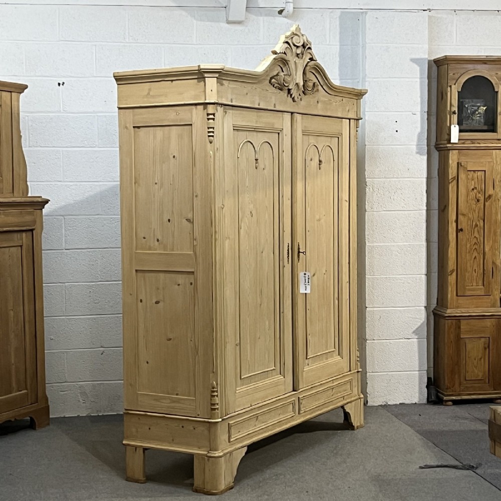 A large late nineteenth-century natural pine double wardrobe featuring a carved scroll pediment, arched door mouldings, and a flat plinth base. View III