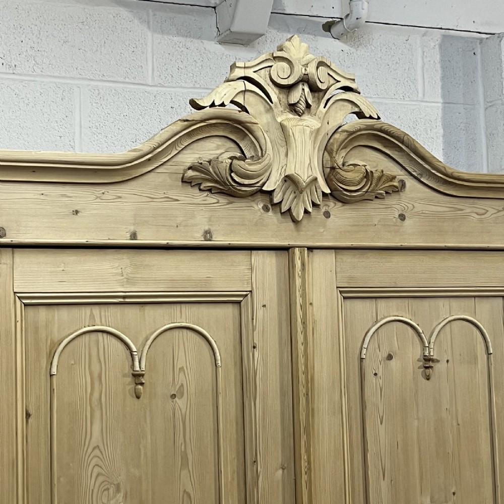 A large late nineteenth-century natural pine double wardrobe featuring a carved scroll pediment, arched door mouldings, and a flat plinth base. View V