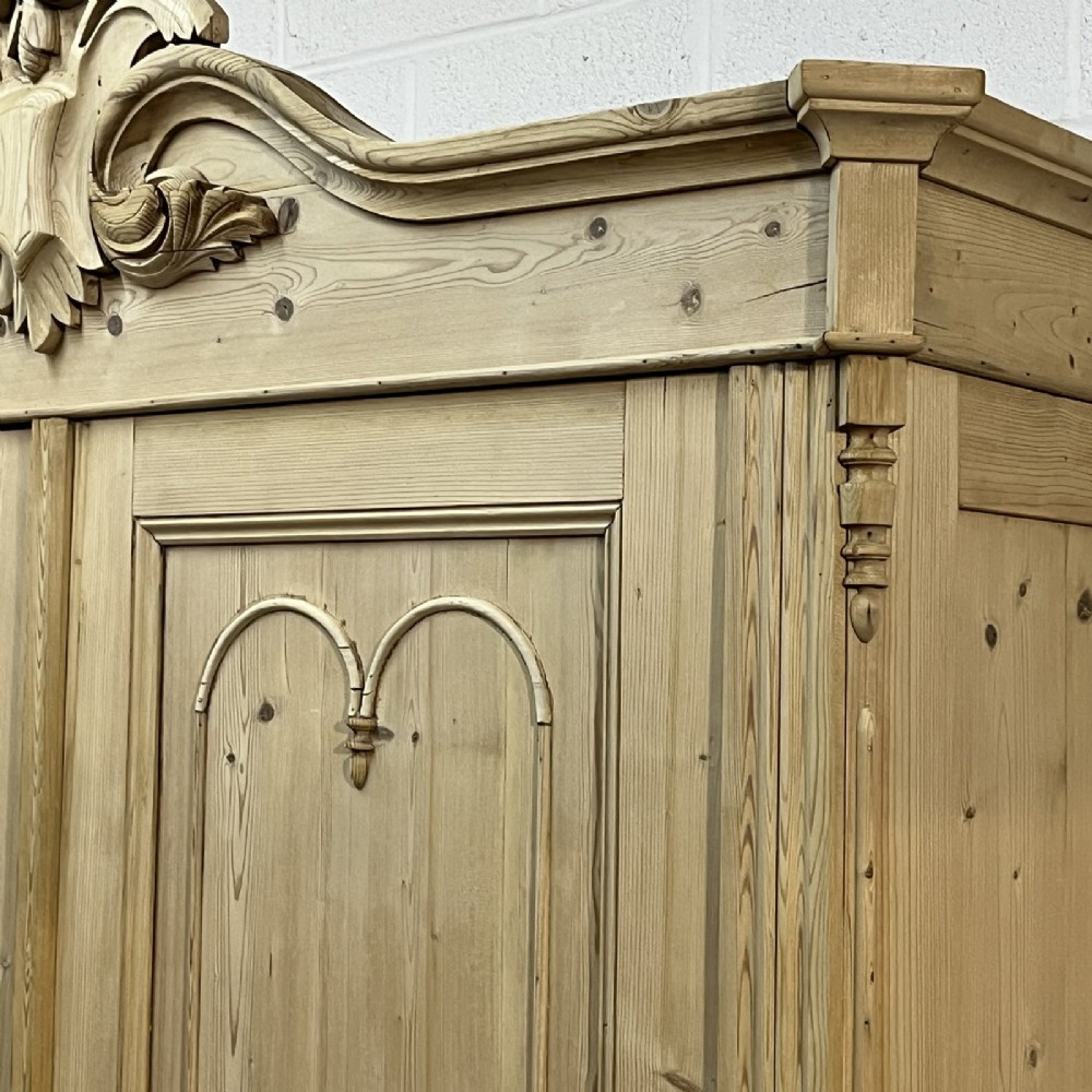 A large late nineteenth-century natural pine double wardrobe featuring a carved scroll pediment, arched door mouldings, and a flat plinth base. View VI