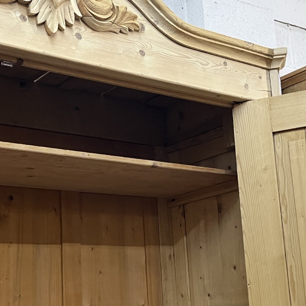A large late nineteenth-century natural pine double wardrobe featuring a carved scroll pediment, arched door mouldings, and a flat plinth base. View IX