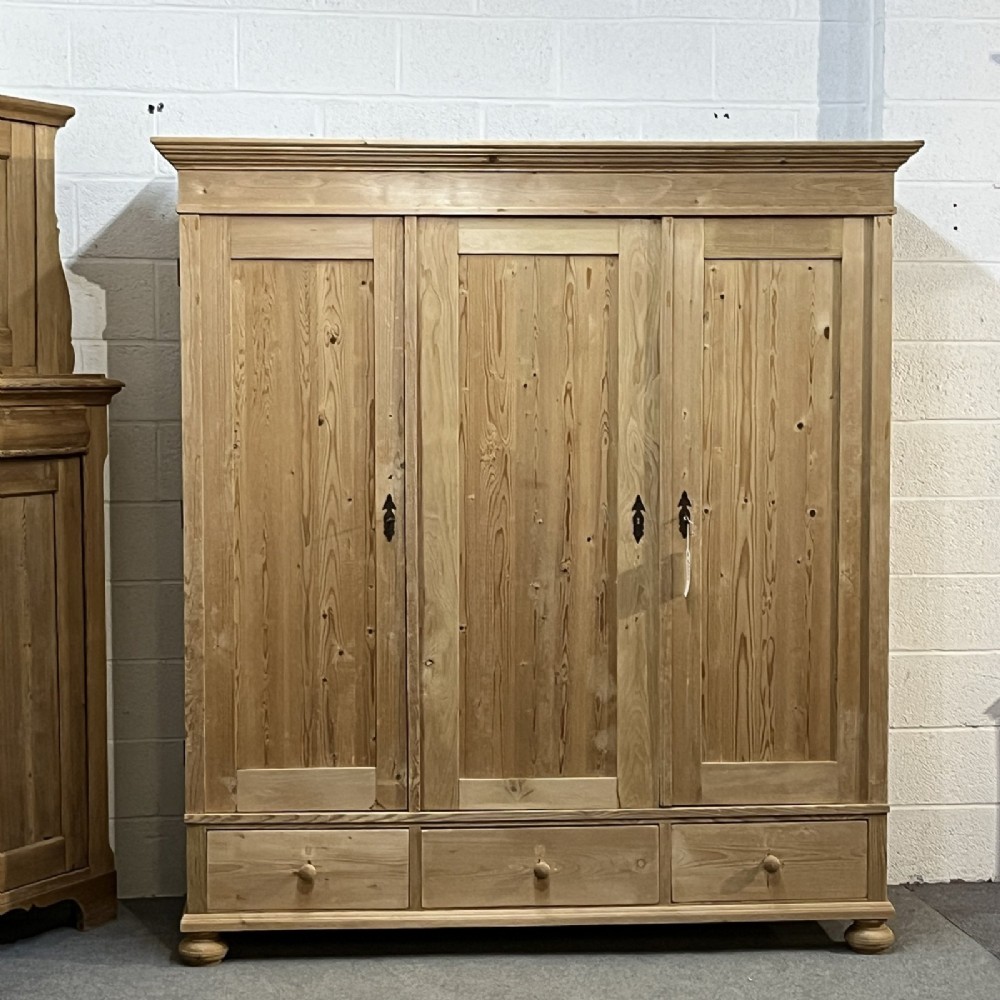 A large natural pine triple wardrobe featuring three vertical panelled doors above three aligned base drawers with turned wooden knobs.