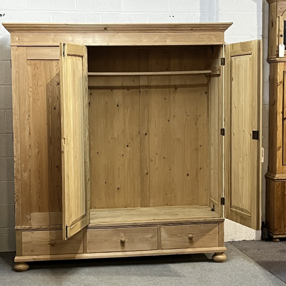 A large natural pine triple wardrobe featuring three vertical panelled doors above three aligned base drawers with turned wooden knobs. View II