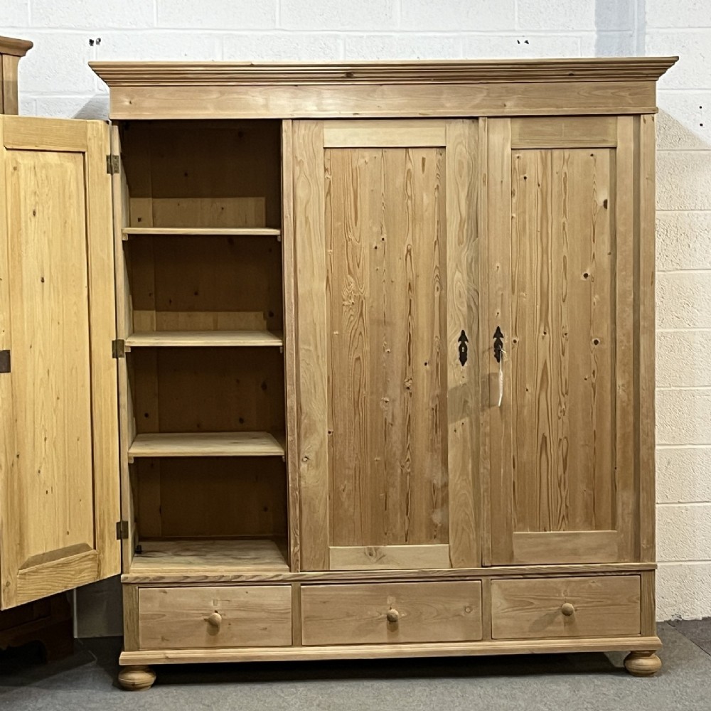 A large natural pine triple wardrobe featuring three vertical panelled doors above three aligned base drawers with turned wooden knobs. View IV
