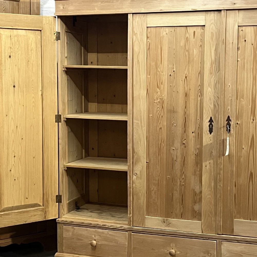 A large natural pine triple wardrobe featuring three vertical panelled doors above three aligned base drawers with turned wooden knobs. View V