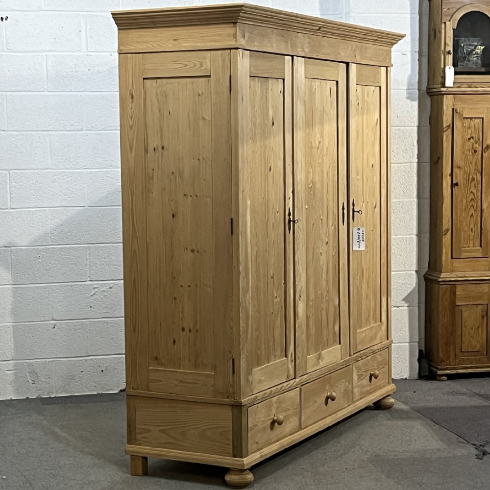 A large natural pine triple wardrobe featuring three vertical panelled doors above three aligned base drawers with turned wooden knobs. View VII