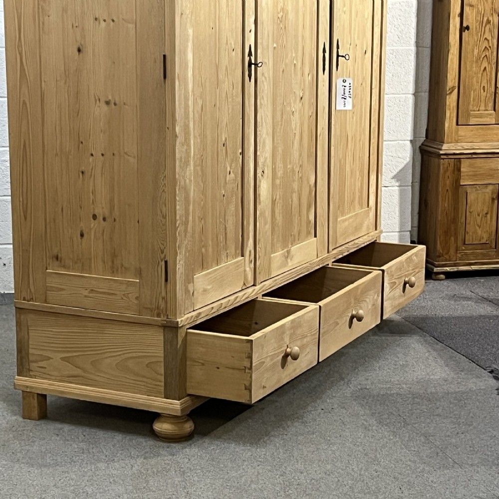 A large natural pine triple wardrobe featuring three vertical panelled doors above three aligned base drawers with turned wooden knobs. View VIII