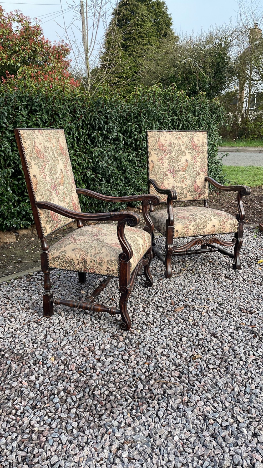 A pair of carved oak high-backed throne armchairs upholstered in floral tapestry fabric with scrolling arms and turned stretchers.