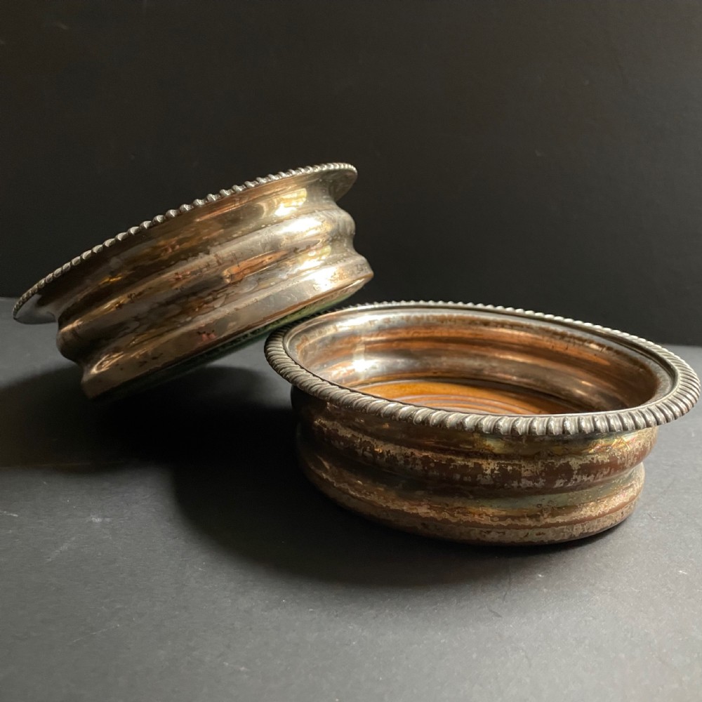 A pair of antique Georgian Old Sheffield Plate wine coasters featuring gadrooned rims and turned wooden bases.
