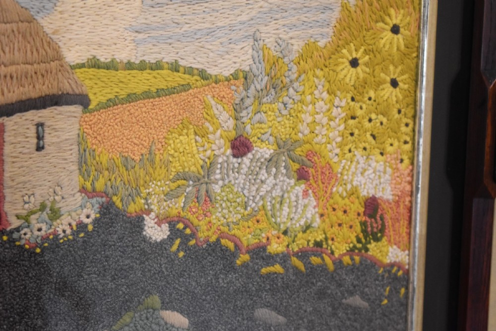 An Arts and Crafts needlework picture depicting a thatched cottage landscape framed in a dark stained wood frame with crossed corner joints. View IV