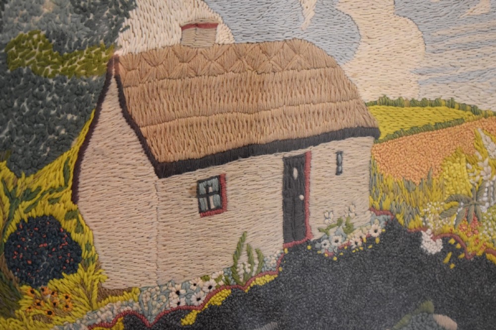 An Arts and Crafts needlework picture depicting a thatched cottage landscape framed in a dark stained wood frame with crossed corner joints. View VI