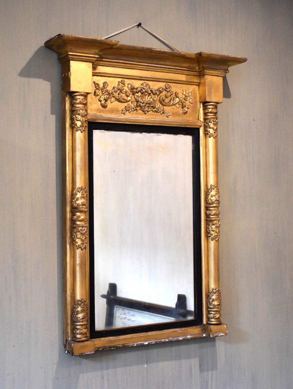A rectangular Regency gilt wall mirror featuring a classical breakfront cornice, carved foliate panel, side pilasters, and an ebonised inner slip.