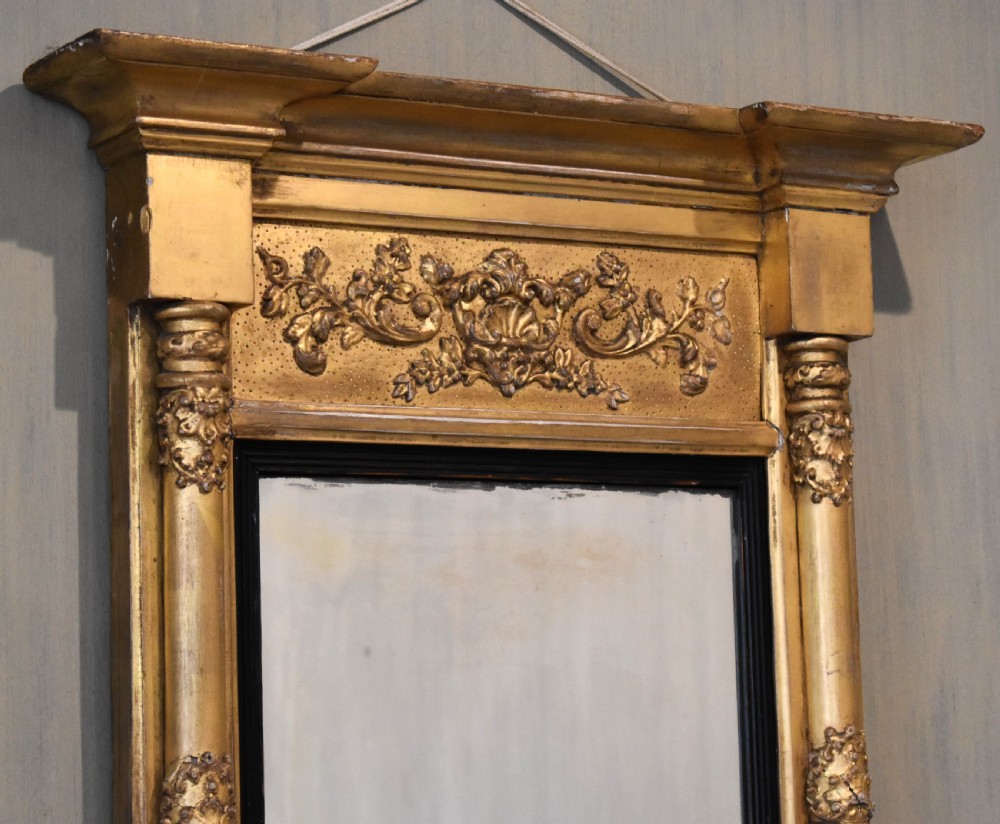 A rectangular Regency gilt wall mirror featuring a classical breakfront cornice, carved foliate panel, side pilasters, and an ebonised inner slip. View III