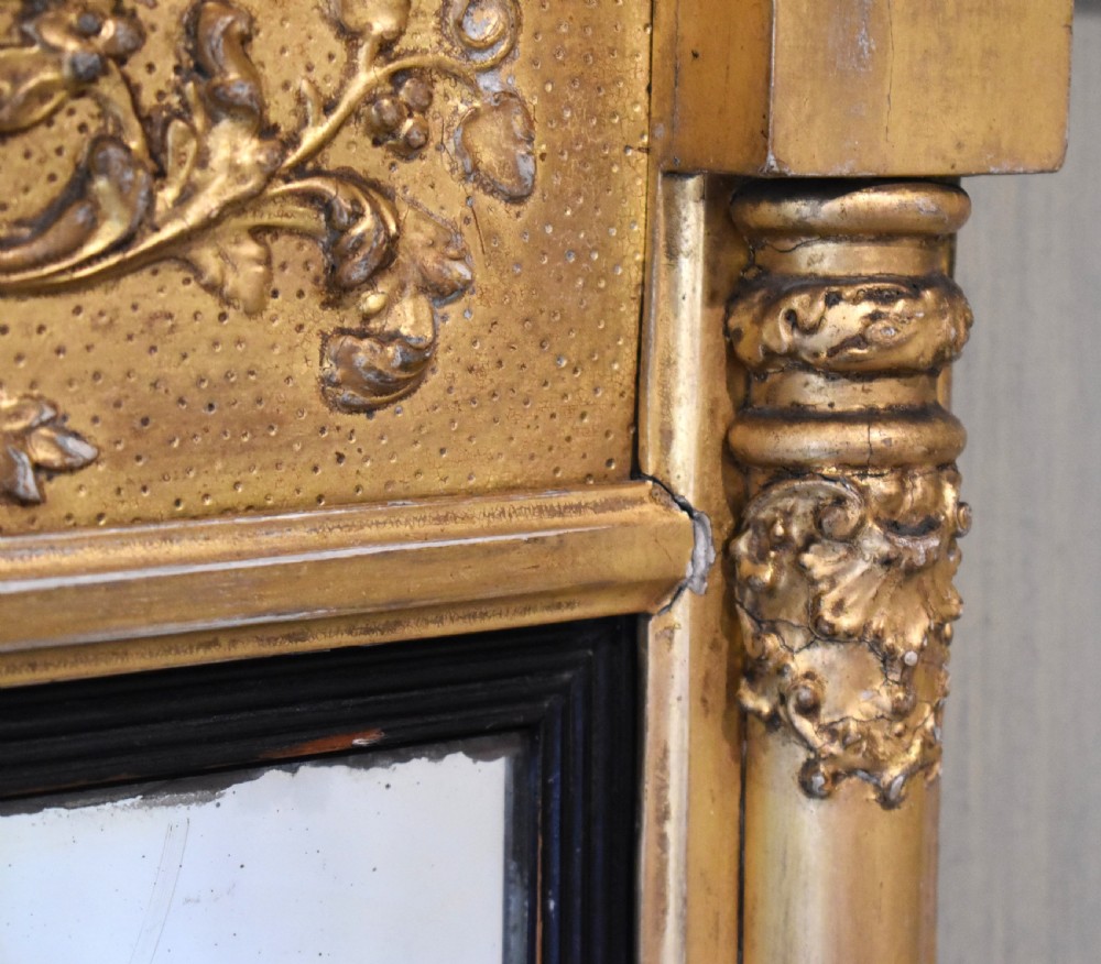 A rectangular Regency gilt wall mirror featuring a classical breakfront cornice, carved foliate panel, side pilasters, and an ebonised inner slip. View IV