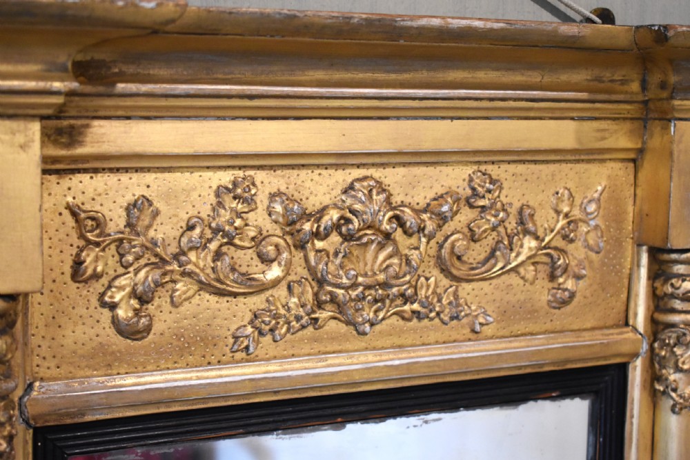 A rectangular Regency gilt wall mirror featuring a classical breakfront cornice, carved foliate panel, side pilasters, and an ebonised inner slip. View V