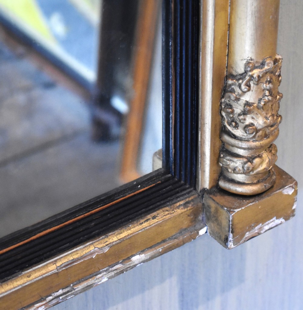 A rectangular Regency gilt wall mirror featuring a classical breakfront cornice, carved foliate panel, side pilasters, and an ebonised inner slip. View VII