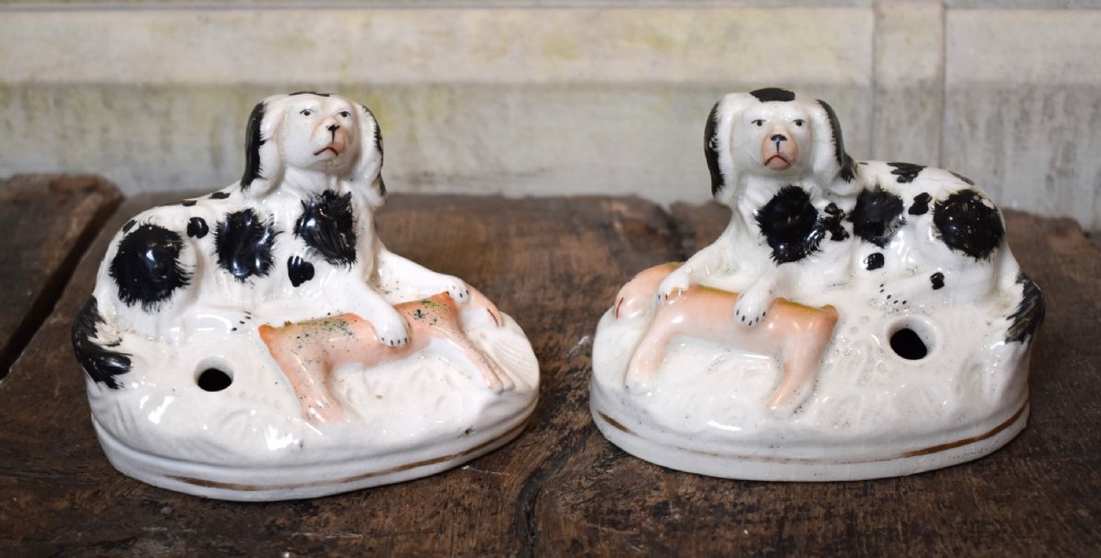 A pair of antique Staffordshire earthenware quill holders depicting black and white reclining spaniels with game at their paws on oval bases.