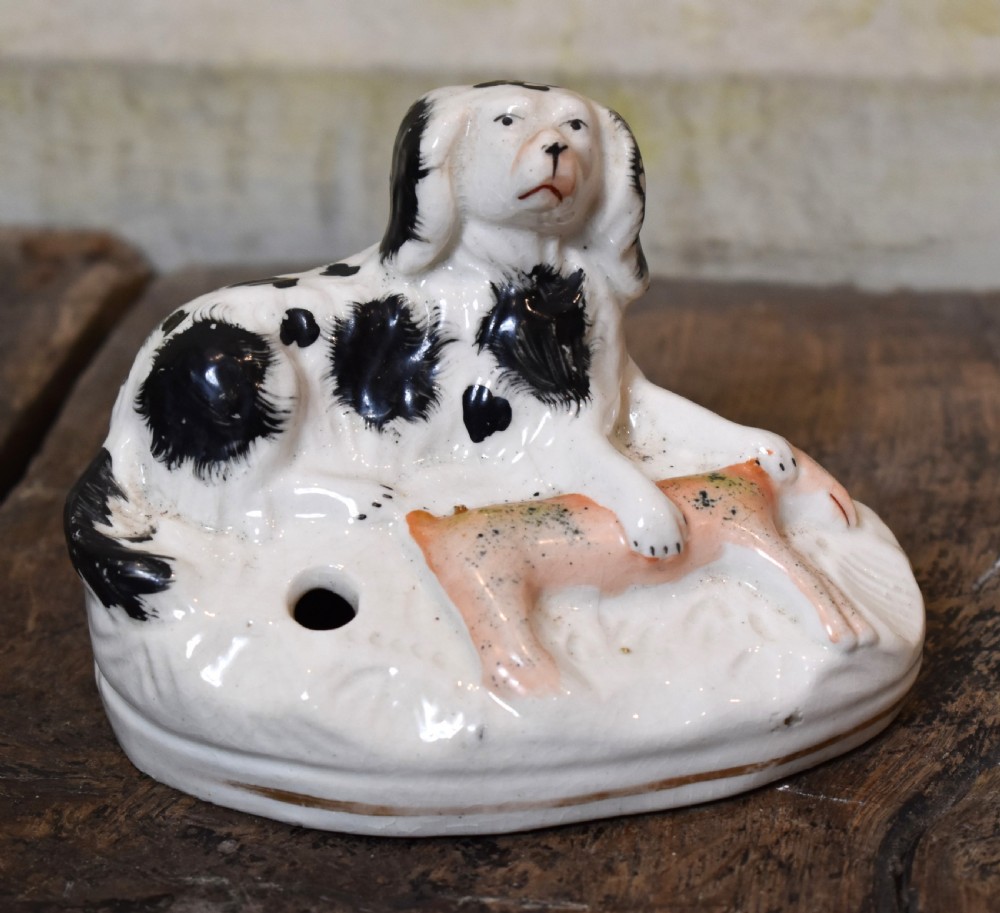 A pair of antique Staffordshire earthenware quill holders depicting black and white reclining spaniels with game at their paws on oval bases. View II