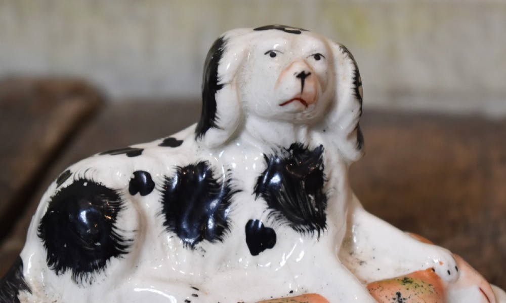 A pair of antique Staffordshire earthenware quill holders depicting black and white reclining spaniels with game at their paws on oval bases. View IV