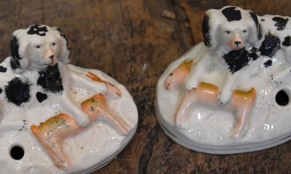 A pair of antique Staffordshire earthenware quill holders depicting black and white reclining spaniels with game at their paws on oval bases. View V