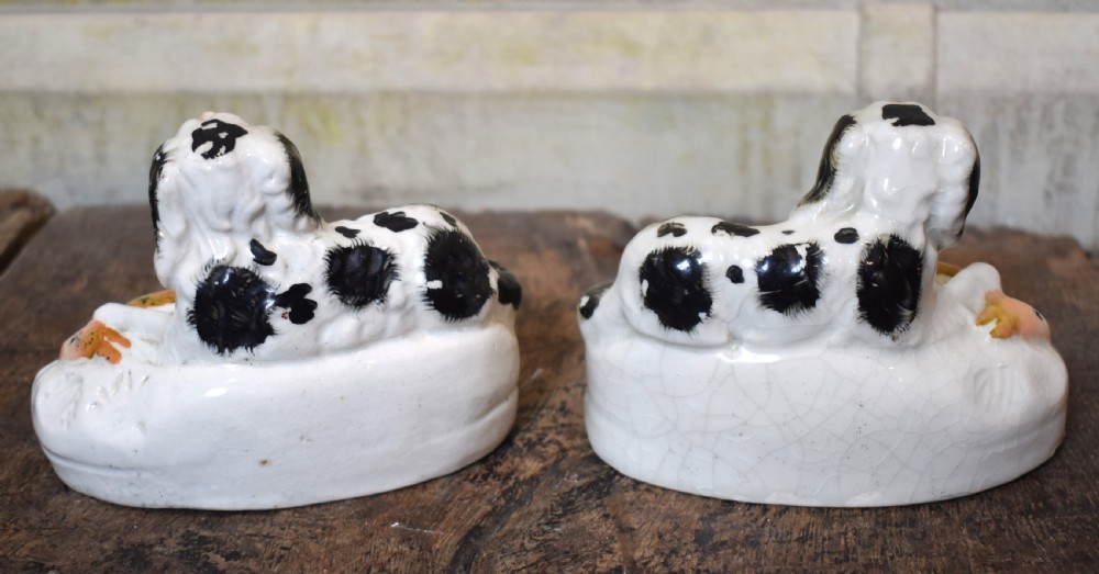 A pair of antique Staffordshire earthenware quill holders depicting black and white reclining spaniels with game at their paws on oval bases. View VI