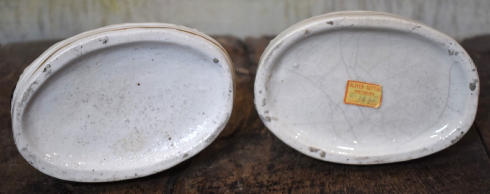 A pair of antique Staffordshire earthenware quill holders depicting black and white reclining spaniels with game at their paws on oval bases. View VII
